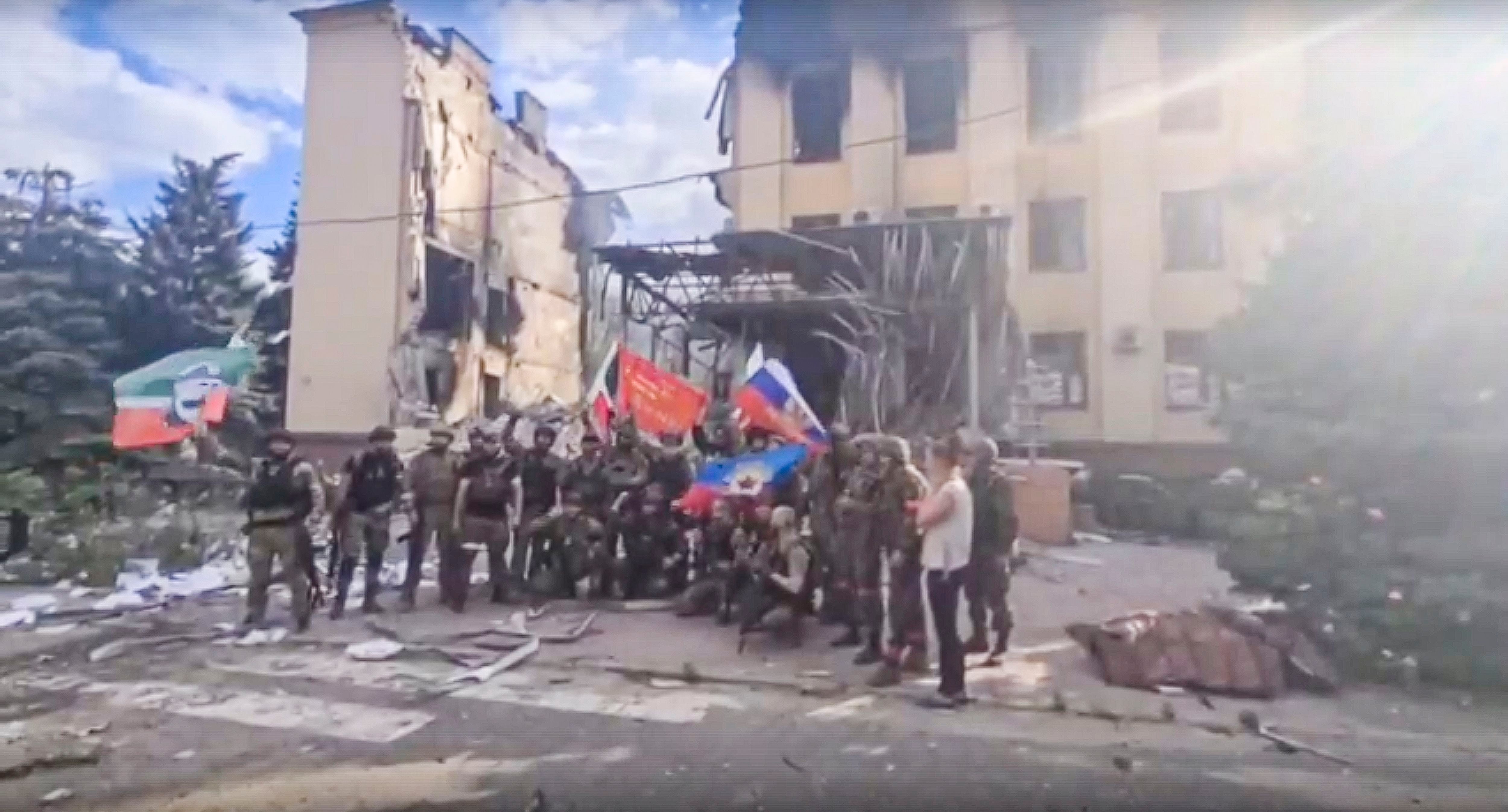 This photo taken from video provided by Ramzan Kadyrov's Official Telegram channel released on Saturday, July 2, 2022, shows Russian troops including soldiers of Chechen regiment waving Russian and Chechen republic national flags as they pose for a photo in front of a destroyed building in Lysychansk, Ukraine. (Ramzan Kadyrov's Official Telegram channel via AP, File)