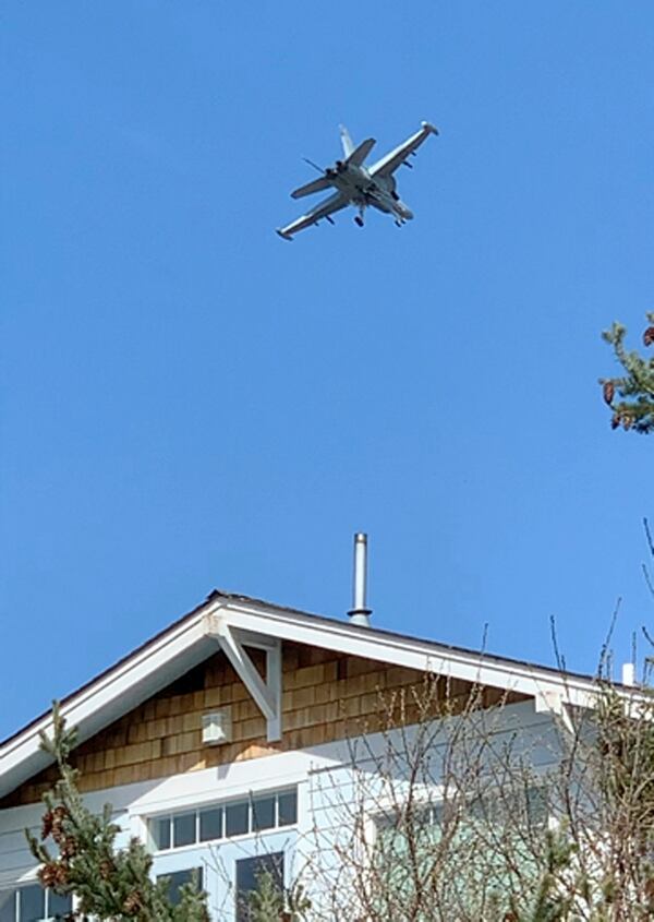 This March 28, 2019 photo from video provided by Whidbey Island resident Bradley Portin shows a Navy jet roaring above the home of his neighbors Marge Plecki and Michael King in Coupeville, Wash. Portin, Plecki and King are among three dozen residents who filed a federal lawsuit against the Navy last week, saying the incessant noise from expanded flight training operations at a small nearby landing strip have cost them the use of their properties and made their lives miserable. (Bradley Portin via AP)