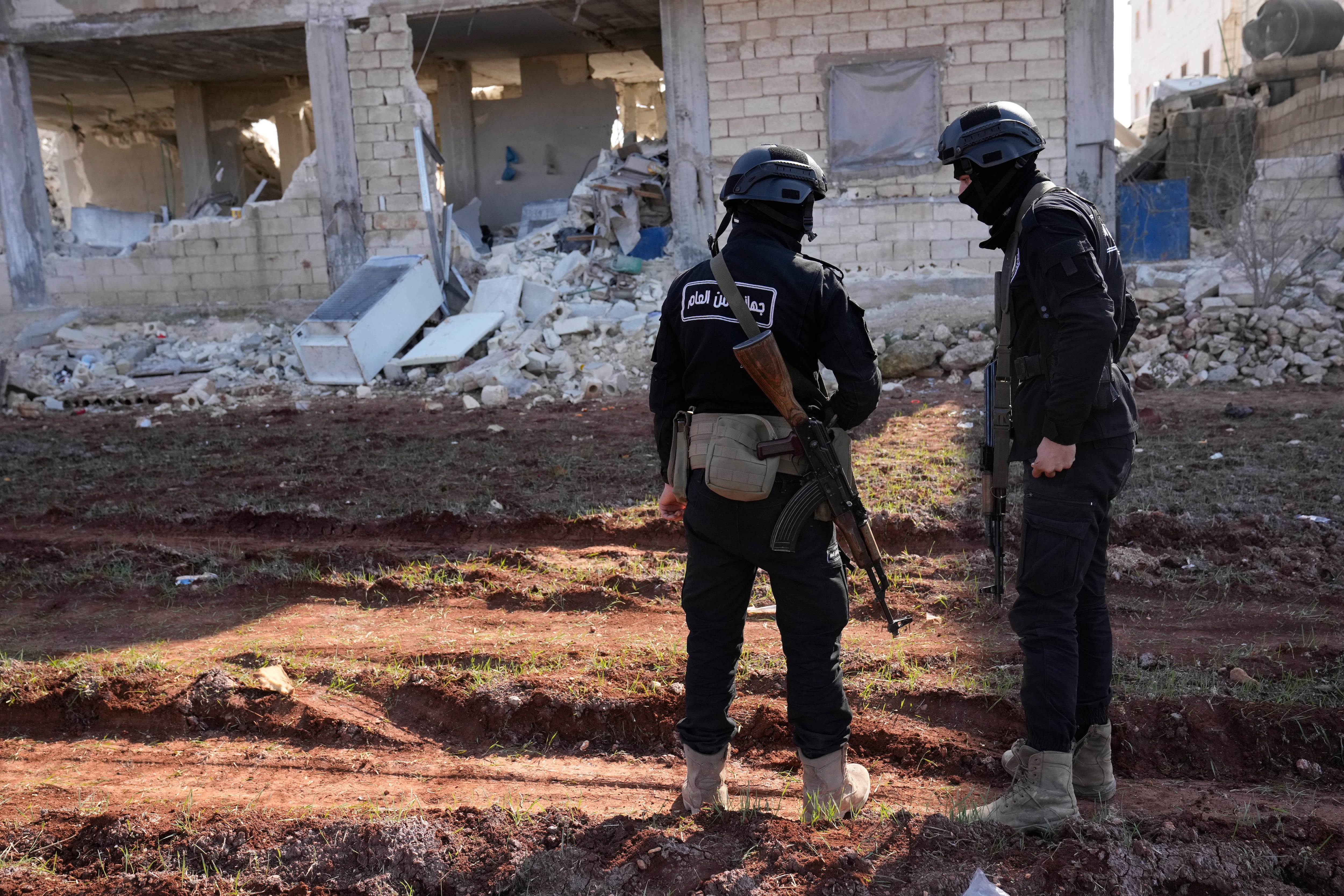 Militants of the al-Qaida-linked Hayat Tahrir al-Sham organization stand in front of a destroyed house in Atareb, Syria, Sunday, Feb. 12, 2023.