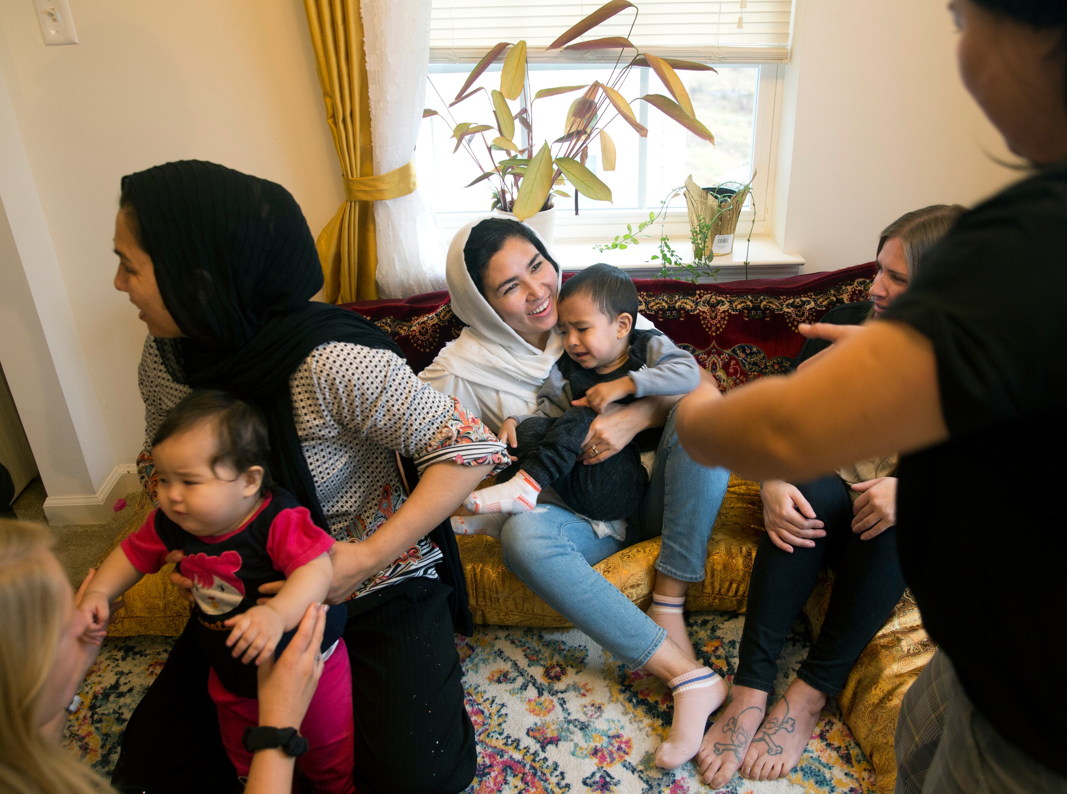 Sima Gul, center, holds her son, Amir Mazlom Yar, as Azizgul Ahmadi, right, reaches for him during a gathering at her home, welcoming Gul to Blacksburg, Va., on Dec.9, 2022.