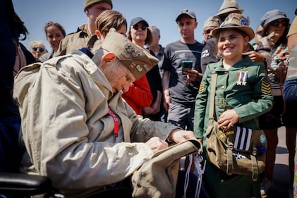 A U.S. veteran signs the bag of a World War II enthusiast during a gathering in preparation of the 79th D-Day anniversary in Sainte-Mere-Eglise Normandy, France, Sunday, June 4, 2023.