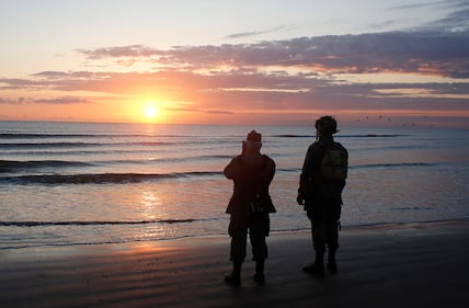 World War II re-enactors stand looking out to sea on Omaha Beach in Normandy, France