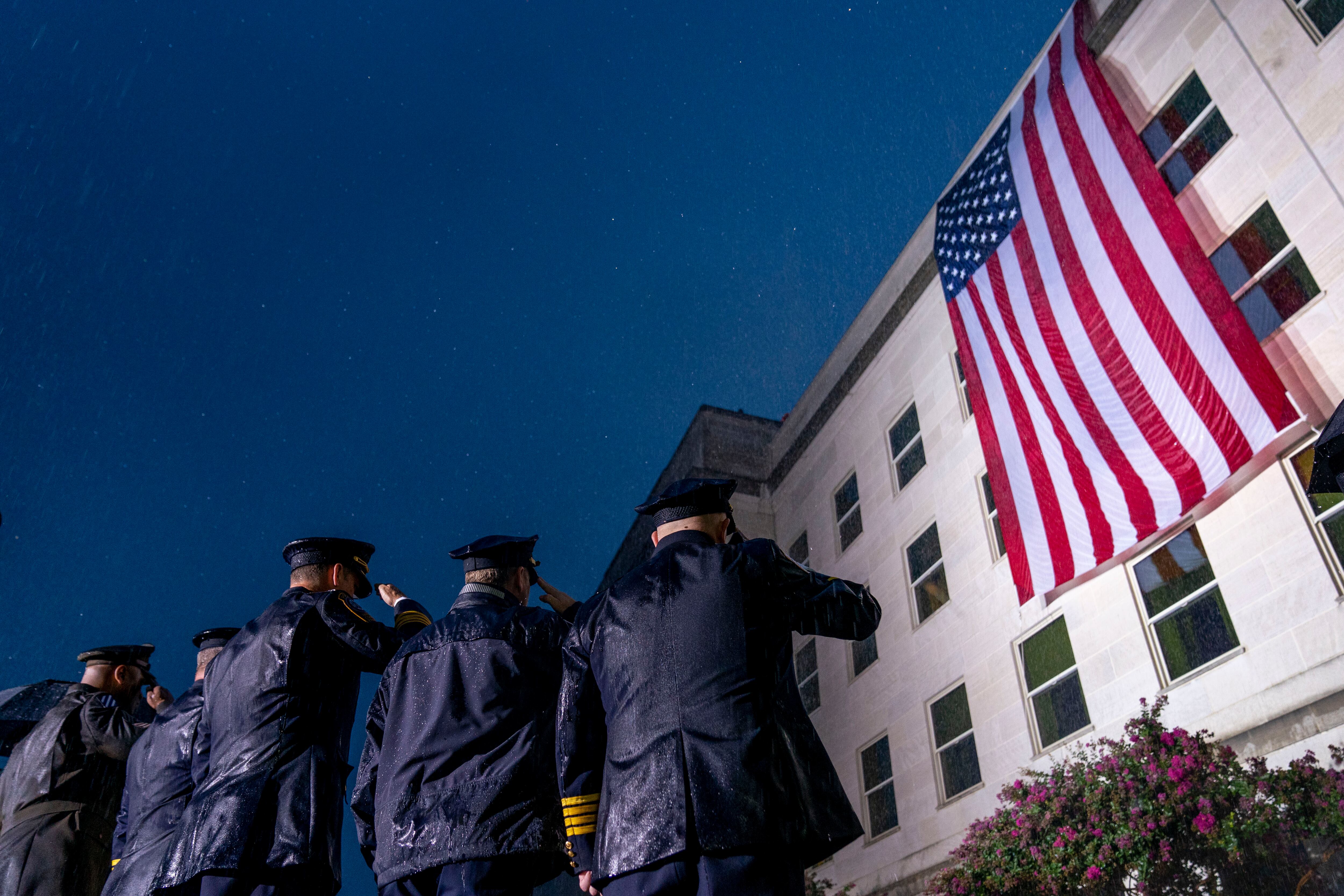 First responders salute in a driving rain as a U.S. flag is unfurled at the Pentagon in Washington, Sunday, Sept. 11, 2022, at sunrise on the morning of the 21st anniversary of the 9/11 terrorist attacks.