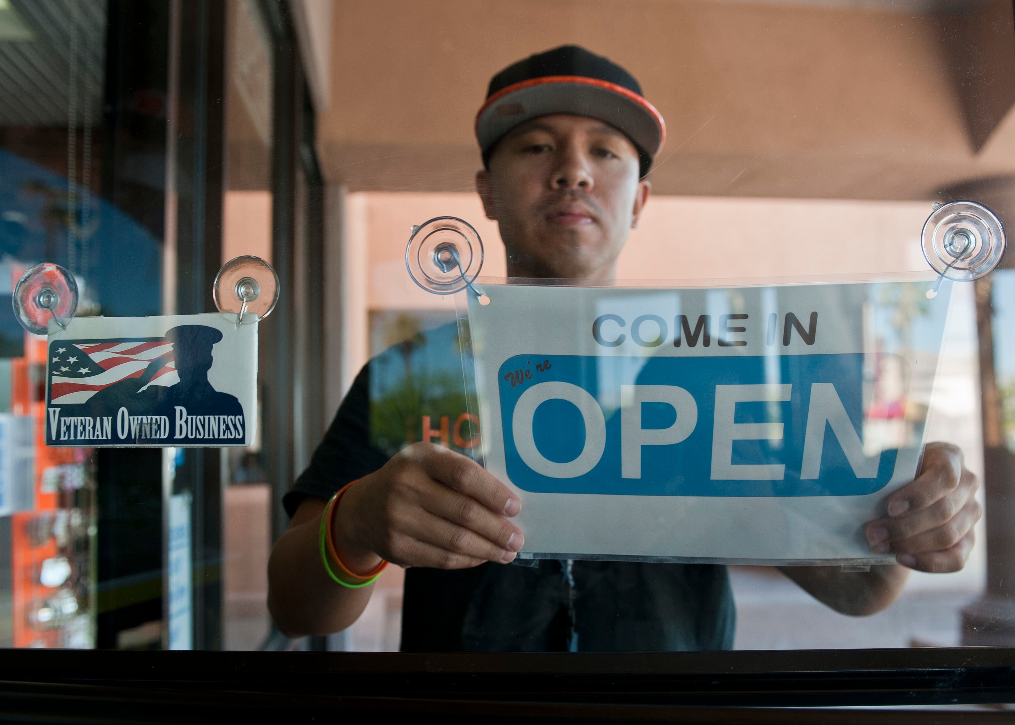 A veteran who started a small business after leaving the Air Force flips the open sign to his retail store in Las Vegas, June 22, 2015.