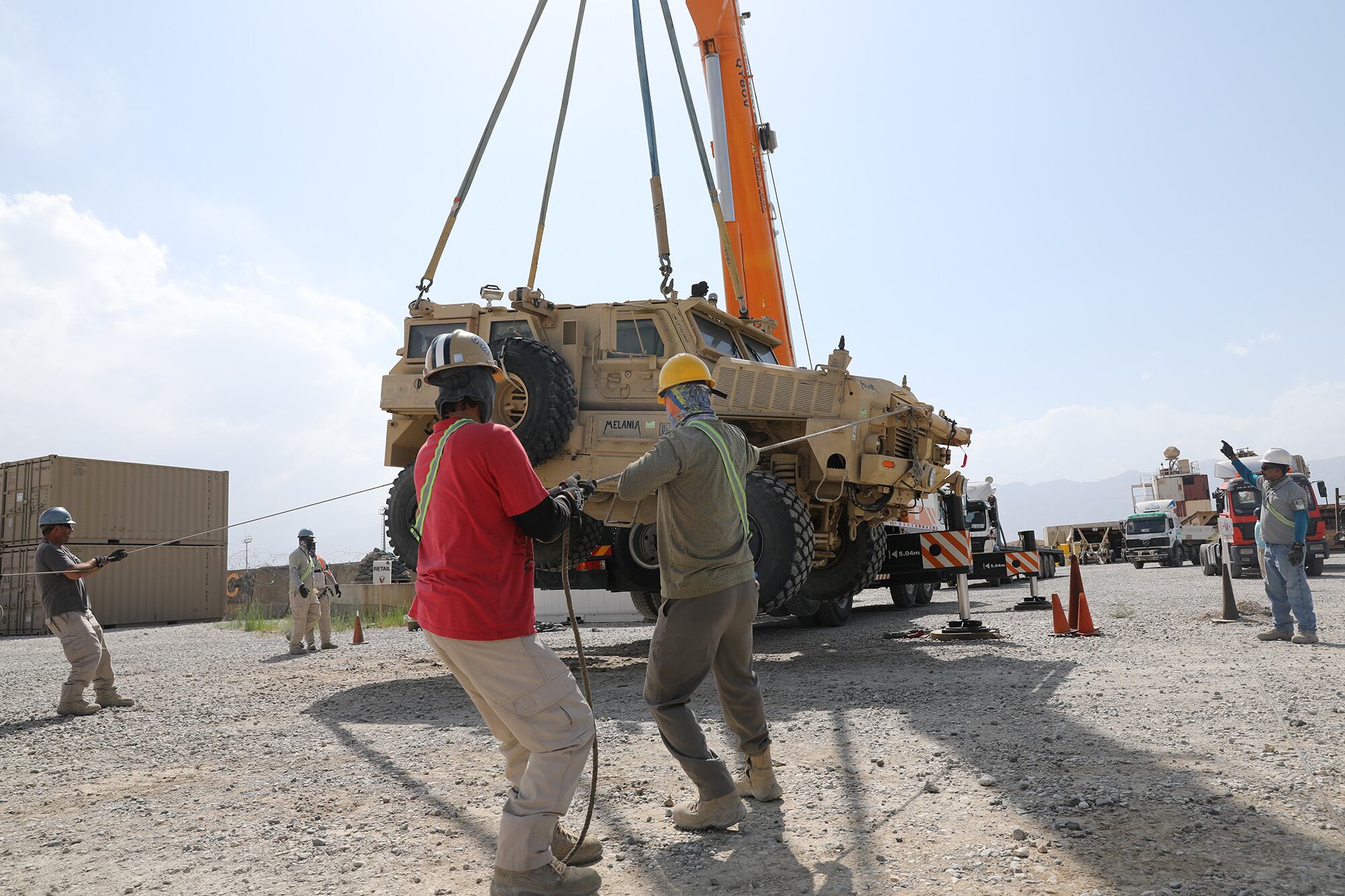 Civilian contractors prepare to load a Mine Resistant Ambush Protected vehicle on to a flatbed trailer during the retrograde cargo operation on Bagram Air Field, Afghanistan, July 12, 2020.