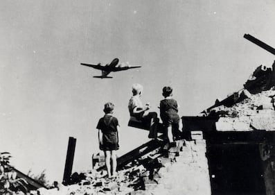 Children look on as a plane flies overhead. In 1948, the U.S. reportedly delivered some 13,000 tons of cargo and took off more than 89,000 times, totaling more than 600,000 hours of flight.