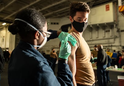 Aviation Ordnanceman Airman Michael Beatty, right, receives an influenza vaccine from Hospitalman Glenda Martinez on Nov. 20, 2020, in the hangar bay of the aircraft carrier USS Carl Vinson (CVN 70) in the Pacific Ocean.