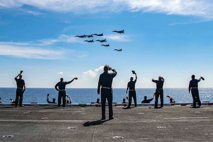 Master Chief David Conduff, command master chief of the aircraft carrier USS Nimitz (CVN 68), waves to four F-18's from the Nimitz and four MiG 29K Fulcrum K from the Indian navy aircraft carrier INS Vikramaditya (R 33) on Nov. 20, 2020, from the flight deck of the Nimitz while participating in Malabar 2020 in the Indian Ocean.