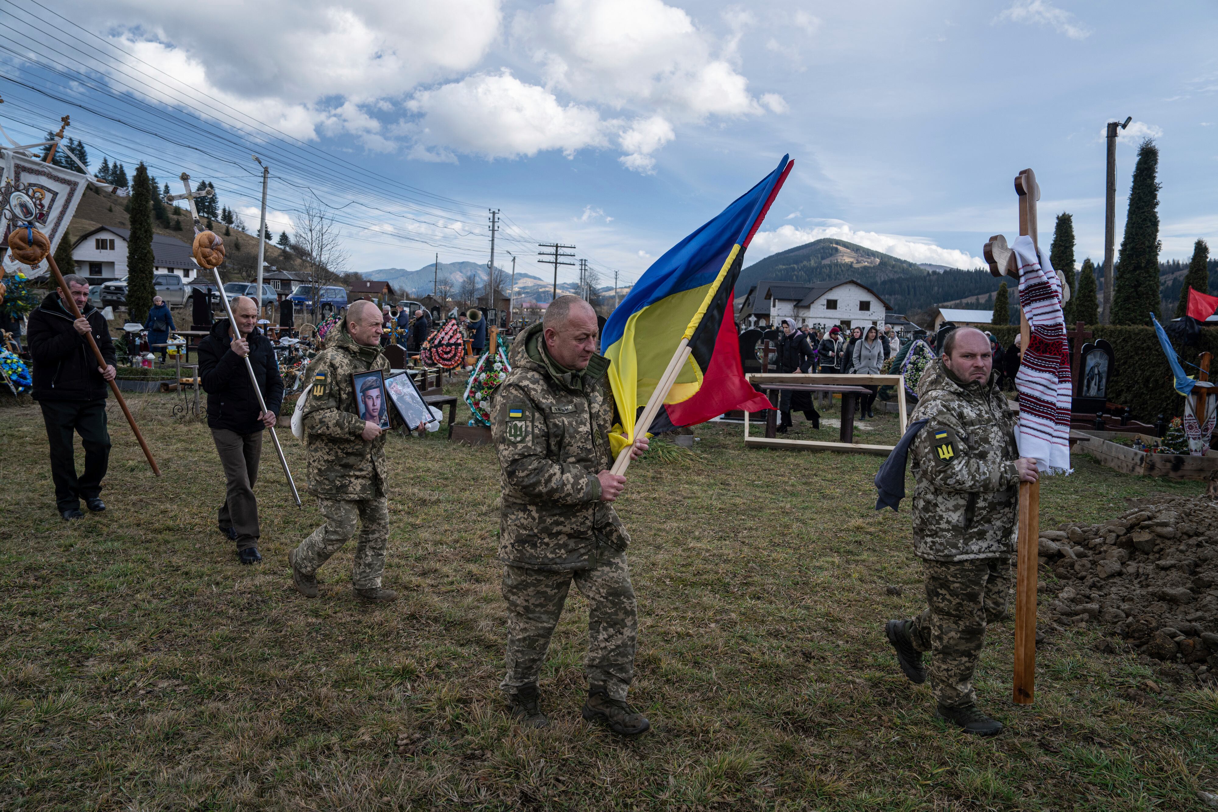 Ukrainian servicemen carry national flags and photos of their comrade Vasyl Boichuk who was killed in Mykolayiv in March 2022, during his funeral ceremony at the cemetery in Iltsi village, Ukraine, Tuesday, Dec. 26, 2023.