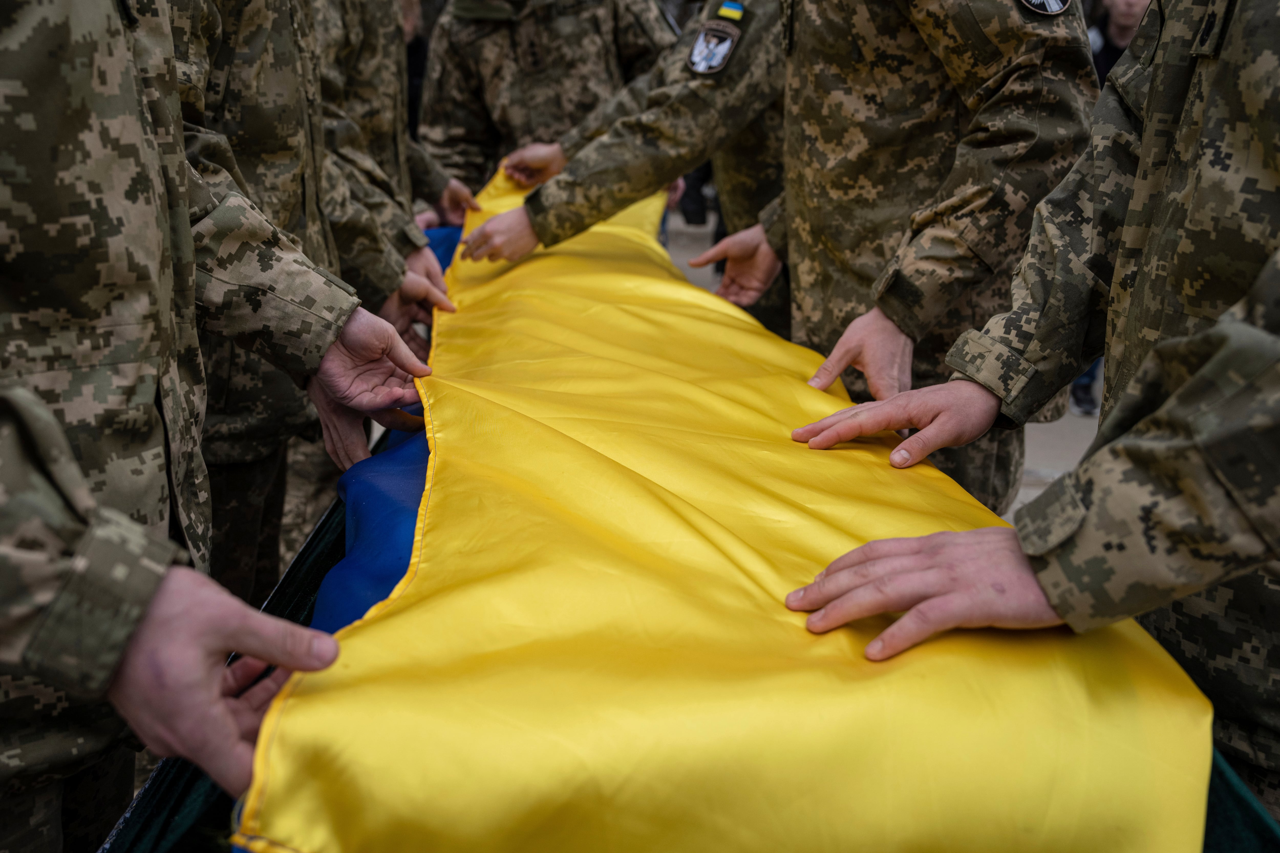 Ukrainian servicemen fold the national flag over the coffin of their comrade Andrii Neshodovskiy during the funeral ceremony in Kyiv, Ukraine, Saturday, March 25, 2023.